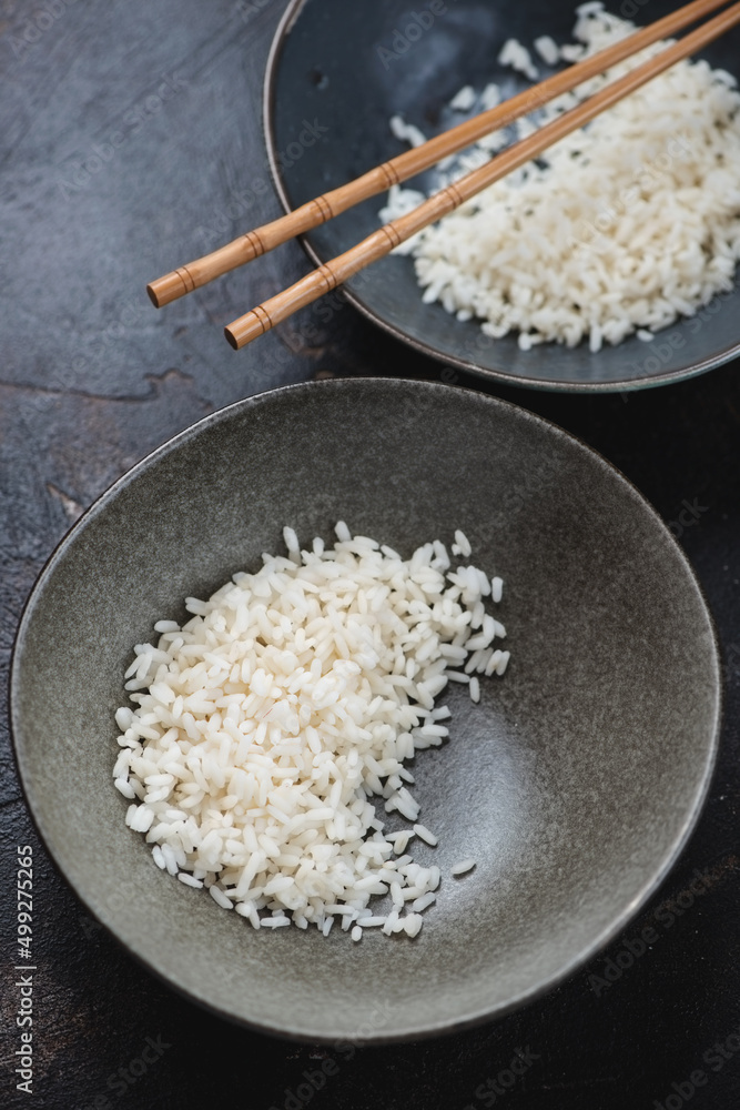 Bowls with steamed rice on a dark-brown stone background, vertical shot, selective focus
