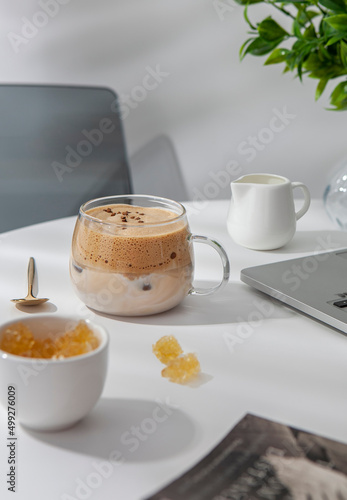 Cup of greek frappe with sugar and jar of milk and laptop on the white table