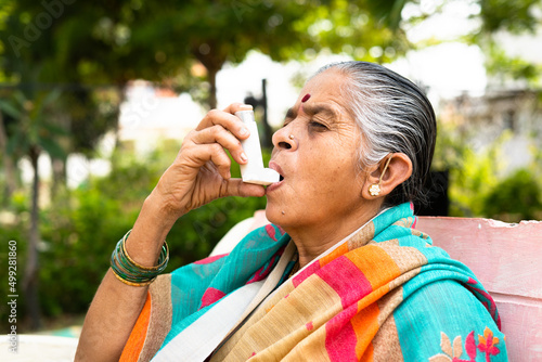 elderly woman using asthma inhaler while sitting at park due to allergy - concept showing effects of pollution, illnes and disease photo