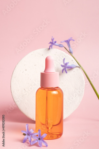 Serum glass bottle with pipette and beautiful flower on pink background. Natural Organic Spa Cosmetic concept. Front view.