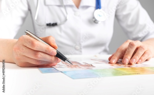 Wallpaper Mural Doctor with stethoscope and pen studying anatomy. Medicine education concept. Woman in lab coat sitting at table and looking at scientific papers. High quality photo Torontodigital.ca