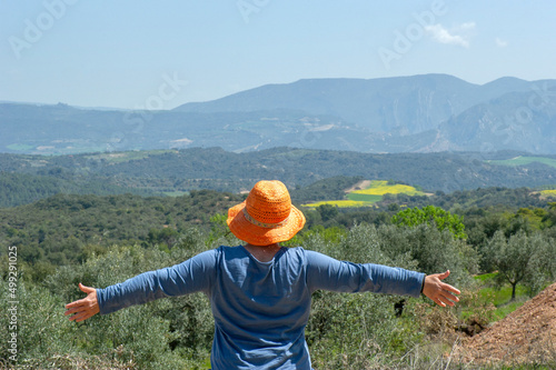 Mujer de espaldas con sombrero de paja naranja y camiseta azul con los brazos en cruz disfrutando de la libertad, la naturaleza, el aire puro y feliz photo