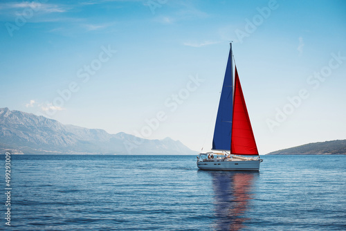 A white yacht with Norwegian flag sails at sea against a background of blue sky and mountains © Maxim Sokolov