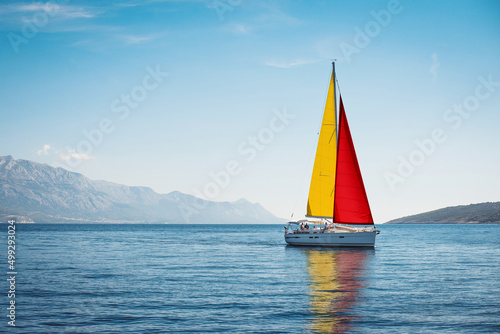 A white yacht with Spanish flag sails at sea against a blue sky and mountains © Maxim Sokolov