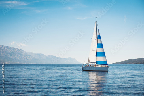 A white yacht with Greek flag sails at sea against the blue sky and mountains © Maxim Sokolov