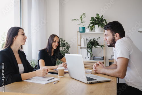 Smiling employees look at each other while working together with laptop at meeting in office