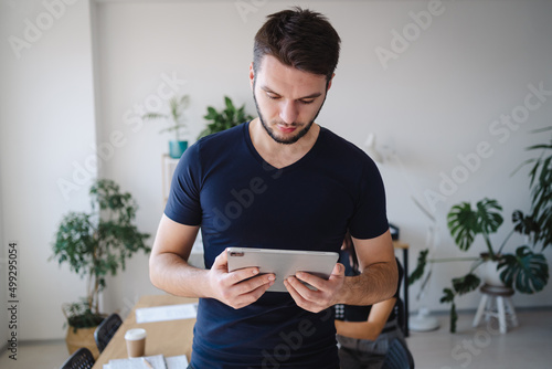 Young businessman wearing casual clothes using tablet, while standing at his office