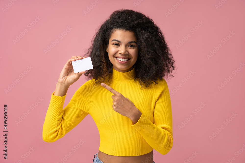 Beautiful smiling curly haired woman holding blank business card pointing finger on copy space isolated on pink background. Mockup, advertisement concept Beautiful smiling curly haired woman holding blank business card pointing finger on copy space isolated on pink background. Mockup, advertisement concept