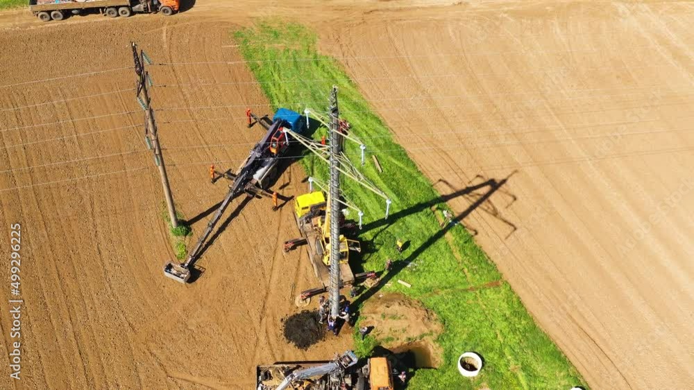 Top view of Installation of power line pylon using construction equipment and workers. Workers are installing an electric pole. Top view of Installation of power line pylon using construction equipment and workers. Workers are installing an electric pole.