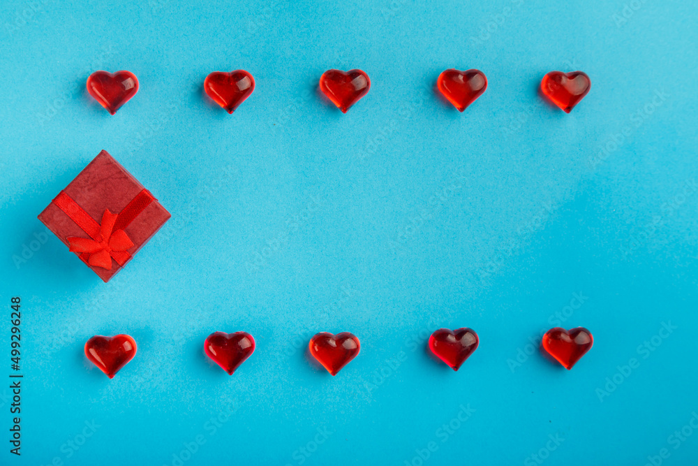 Obraz premium On a blue background, a box with a gift decorated with hearts with red pebbles save a place.