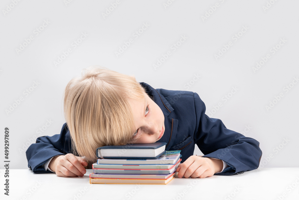 Upset schoolboy with pile of school books and notebooks. Tired or bored boy sleeps at the table. Upset schoolboy with pile of school books and notebooks. Tired or bored boy sleeps at the table.