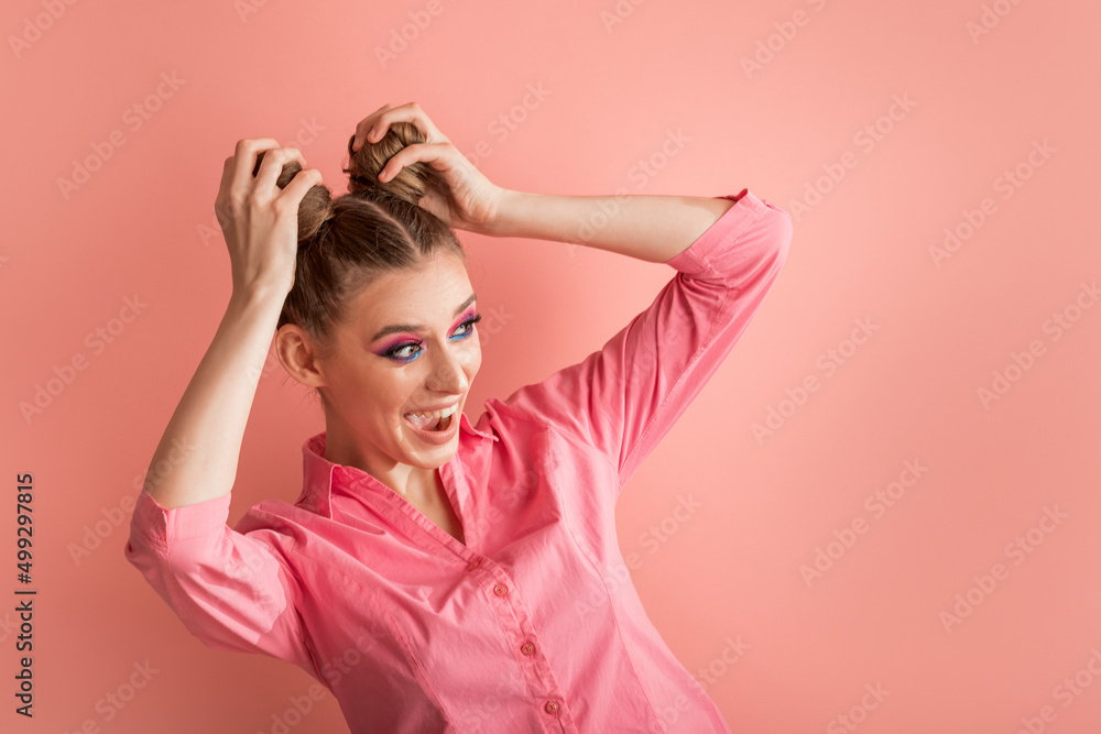 Funny young woman in pink blouse on pink background. Surprised laughing girl with two bun hairstyles looking away. Copy space