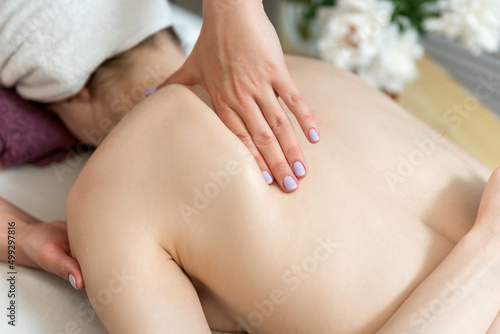 Young woman getting back massage at the spa. Hands of the masseur on the female back.