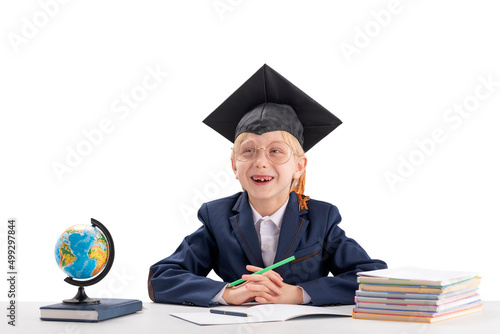 Boy in school uniform and students hat sits at desk and laughs on white background. Education in university college abroad.