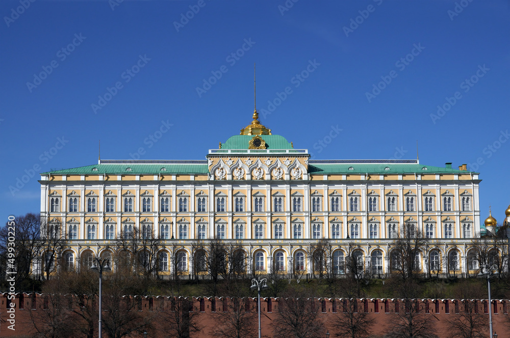 Naklejka premium Grand Kremlin Palace with spire on cupola behinf red brick Kremlin wall cloudless sunny bright day