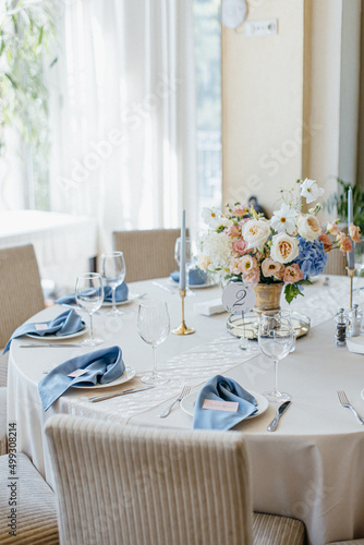 Blue wedding decor. Festive table decorated with flowers on the center, candles, silverware and plates with silk napkins on dusty blue tablecloth