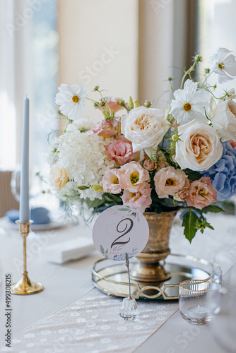 Blue wedding decor. Festive table decorated with flowers on the center, candles, silverware and plates with silk napkins on dusty blue tablecloth