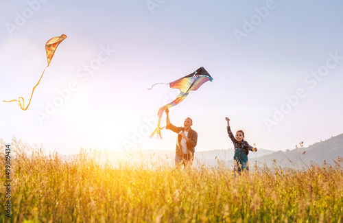 Summer outdoor photo of smiling father with daughter as they releasing colorful kites on the high grass meadow. Warm family moments or outdoor time spending concept image.