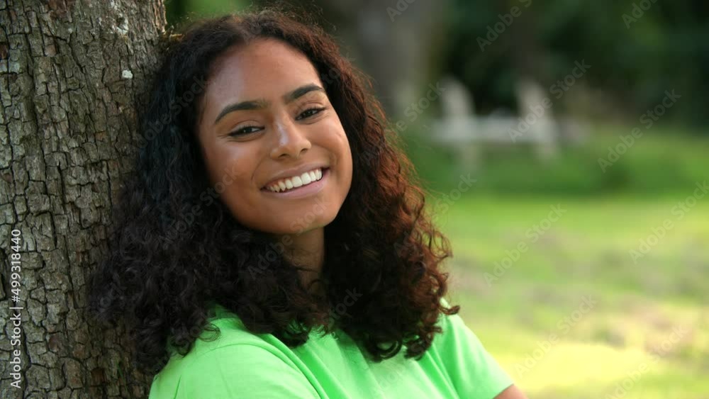 Beautiful mixed race African American girl biracial teenager young woman outside smiling, laughing sitting under a tree in a park or garden Beautiful mixed race African American girl biracial teenager young woman outside smiling, laughing sitting under a tree in a park or garden