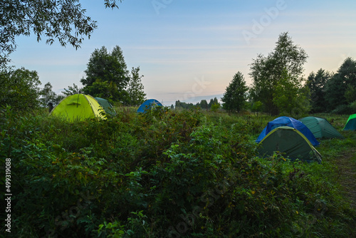 Tourist tents on the background of a summer field at sunrise. Adventure traveling lifestyle. Concept wanderlust. Active weekend vacations wild nature outdoor.
