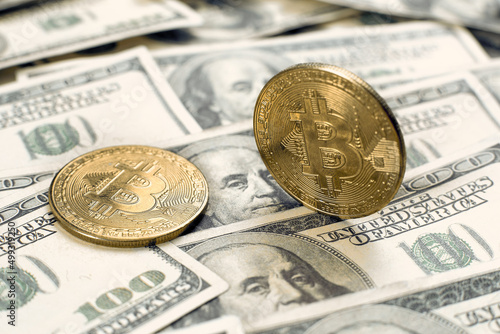 The bitcoin cryptocurrency coin stands on its own end, the second one lies on one hundred dollar bills