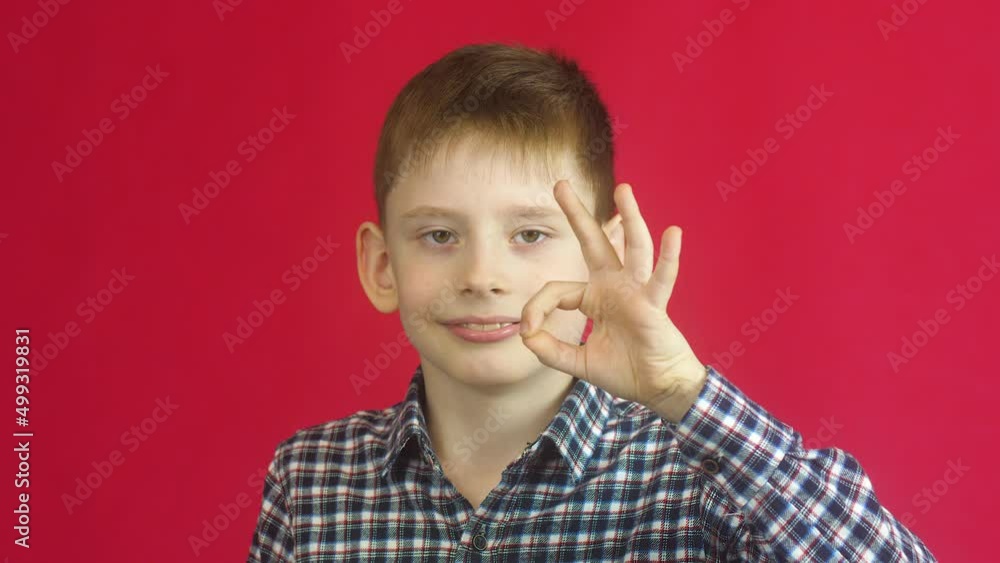 Cheerful caucasian boy 7-8 years old showing thumbs up gesture approx. Sign of consent gesture. A cheerful child is positive. Studio shooting on a red background Cheerful caucasian boy 7-8 years old showing thumbs up gesture approx. Sign of consent gesture. A cheerful child is positive. Studio shooting on a red background