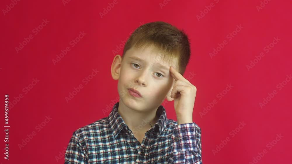 Serious pensive caucasian boy 7 years old looks at the camera meditates.Studio shooting on a red background. Emotions of children. A schoolboy of 8 years old thought about the question Serious pensive caucasian boy 7 years old looks at the camera meditates.Studio shooting on a red background. Emotions of children. A schoolboy of 8 years old thought about the question