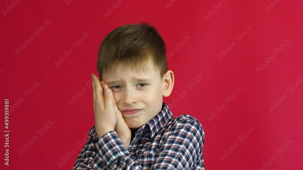 Toothache in a child concept. caucasian boy 7 years old suffers from toothache holding his hands over his mouth. Studio shooting on a red background. Dentistry for children Toothache in a child concept. caucasian boy 7 years old suffers from toothache holding his hands over his mouth. Studio shooting on a red background. Dentistry for children