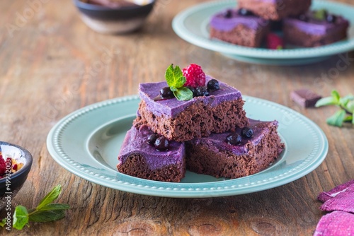 Fototapeta Naklejka Na Ścianę i Meble -  Dessert, sliced chocolate brownies with a layer of ricotta or cream cheese and blueberry puree on a green plate on a brown wooden background. American cuisine.