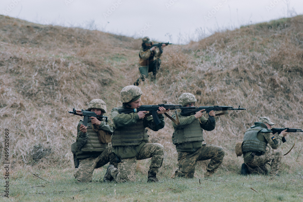 Team of five Ukrainian soldiers aims from kalashnikov assault rifles to russian enemy against background of hill. Team of five Ukrainian soldiers aims from kalashnikov assault rifles to russian enemy against background of hill.
