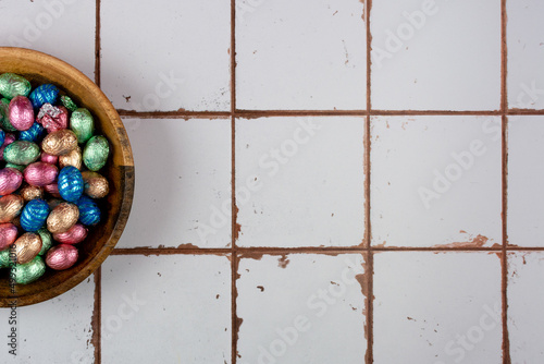 Wooden bowl with pastel colored easter-eggs on tiled backround