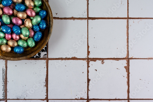 Wooden bowl in a corner with pastel colored easter-eggs on tiled backround