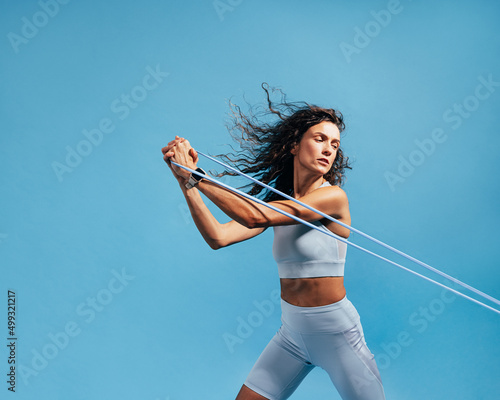 Female athlete working out with stretch bands on blue background. Woman doing intense training using resistance bands. photo