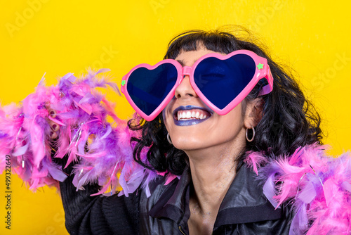 Young woman wears large heart-shaped glasses and a scarf with pink and purple feathers. Beautiful woman has fun at the party. Party concept.