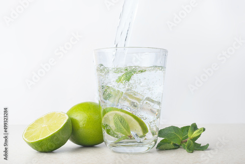 glass of water with ice, lime and mint on a light gray background