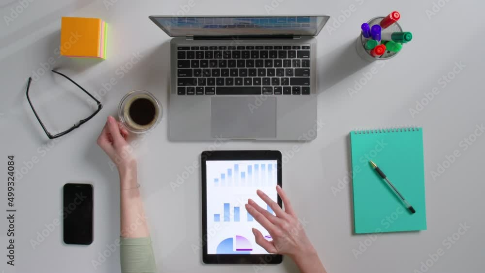 Top view of female scroll tablet screen with chart sitting at desk and drinking coffee Top view of female scroll tablet screen with chart sitting at desk and drinking coffee