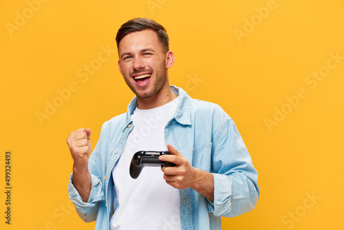 Enjoyed young tanned handsome man in blue basic t-shirt raise fist up hold joystick posing isolated on orange yellow studio background. Copy space Banner Mockup. People lifestyle Lucky winner concept © SHOTPRIME STUDIO
