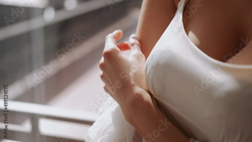 Fragile girl stands by the window in white underwear and nightgown and gently and sexy strokes her hand on the body. Seductive woman with bare shoulder. Good romantic morning for a man
