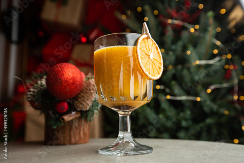 Shiny glass of hot orange grog cocktail served on counter in cafe on new year decoration background photo