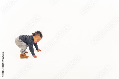 Curious biracial toddler boy trying to stand up in studio over white background. Child development concept. High quality photo