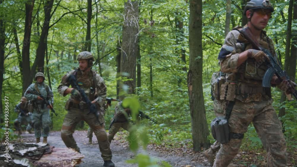 Group of soldiers in full gear a rifle in his hands in dense forest. All run away one soldier falls to the ground. War. Military concept Group of soldiers in full gear a rifle in his hands in dense forest. All run away one soldier falls to the ground. War. Military concept