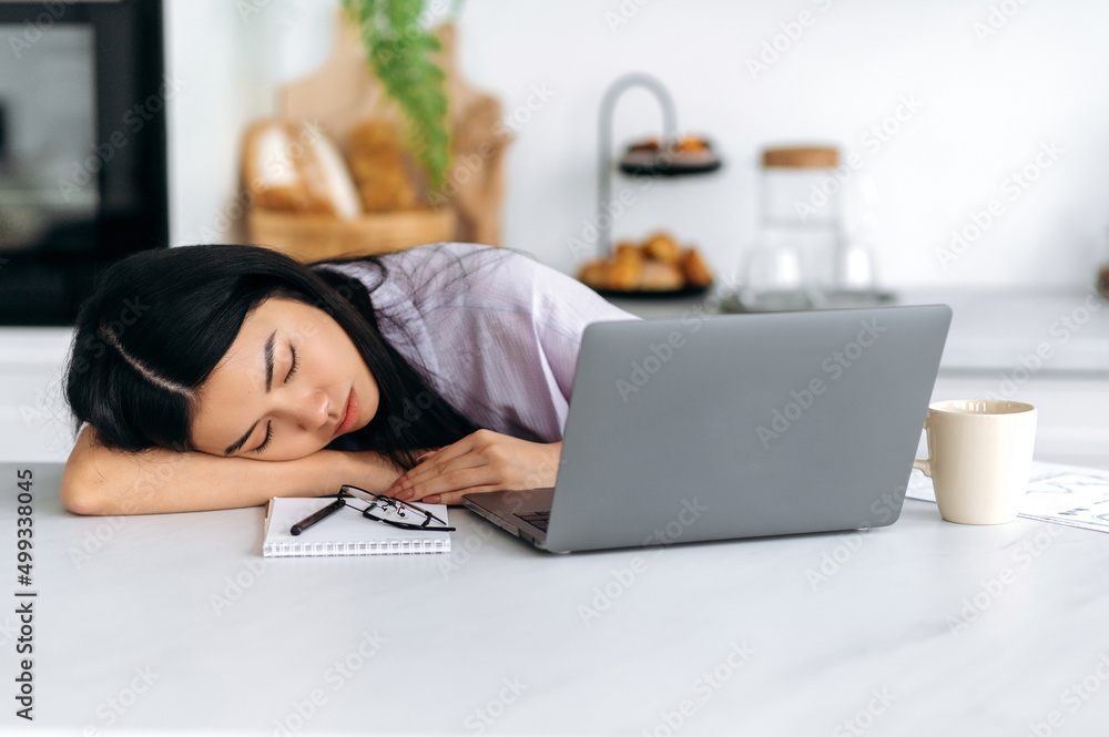 Obraz premium Fatigue concept. Tired exhausted Asian millennial girl, student or freelancer, fell asleep on the table while working remotely or studying in a laptop at home, is overworked, needs rest