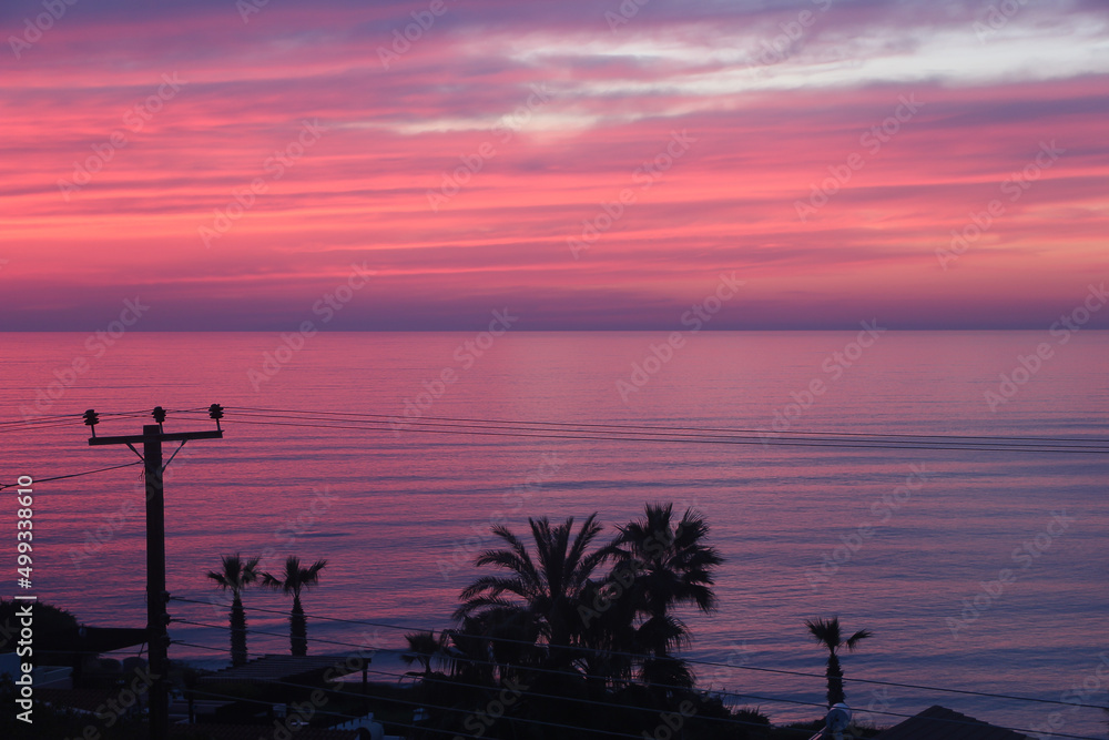 Palm trees beaches and seas on the south cyprus coast as sunset against a red, orange and yellow sky
