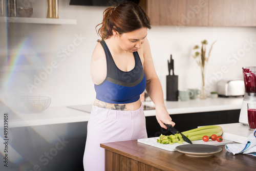 Woman with amputee arm chopping celery at the board and preparing to the healthy dinner photo