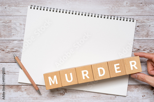 「MURDER」と書かれた積み木、ノート、ペン、手