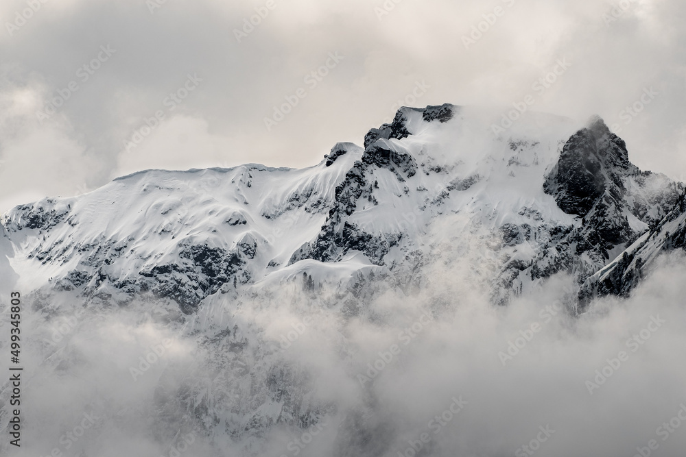 Clouds and fog shroud snow covered mountains and the mountain forests