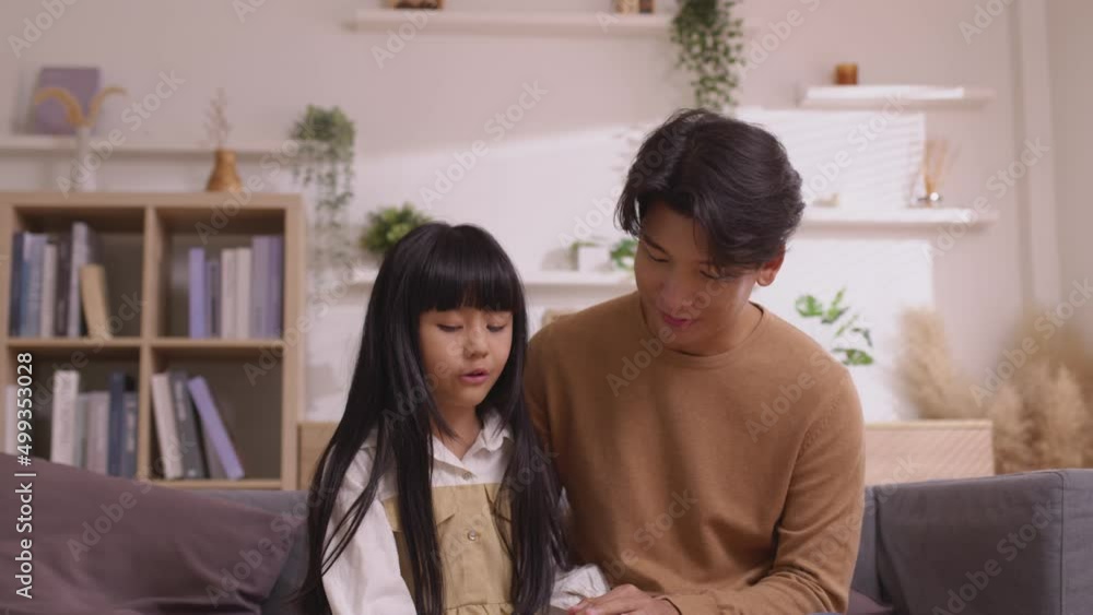 Asian father talking to her baby girl with gentleness while he is resting on her laps on the sofa at home. Asian father talking to her baby girl with gentleness while he is resting on her laps on the sofa at home.