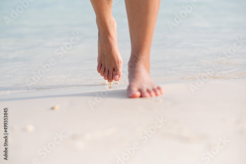 Closeup image of woman with barefoot while walking on the white beach and the sea