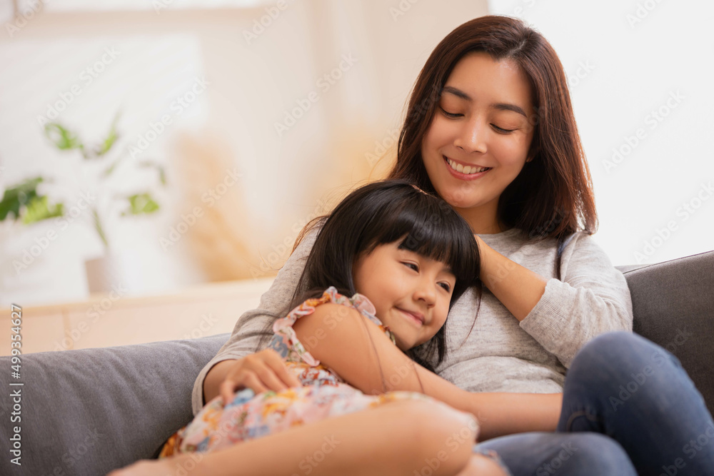 Asian Mum her little daughter hugging sit on sofa smile.Loving family portrait, Mothers Day celebration concept . Asian Mum her little daughter hugging sit on sofa smile.Loving family portrait, Mothers Day celebration concept .