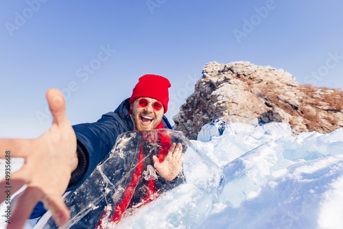 Portrait happy male tourist in red hat with shard of transparent ice in winter on Lake Baikal sunset